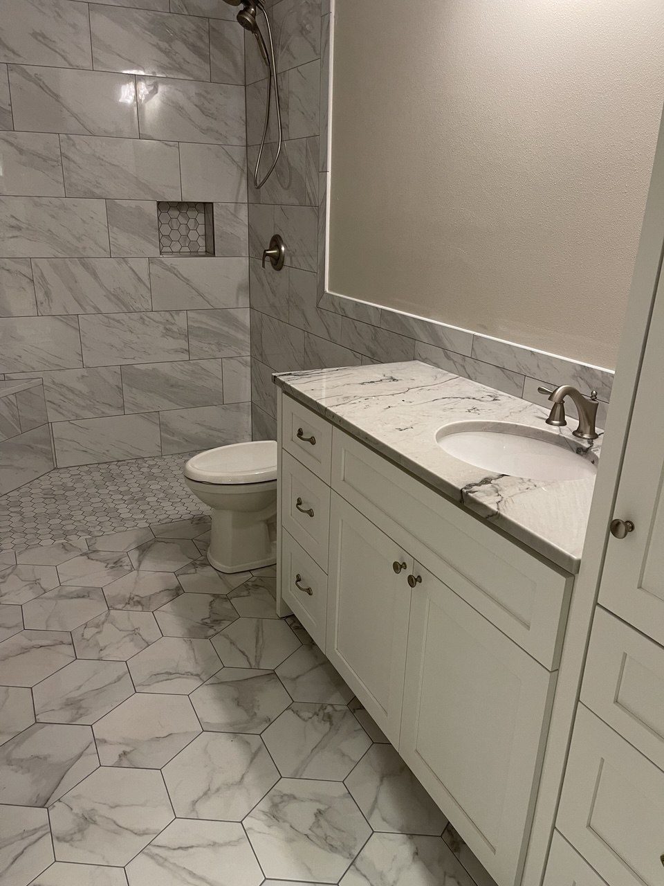 Finished bathroom with a marble-look tiled shower, hexagon tile floor and a white shaker vanity with an undermount sink